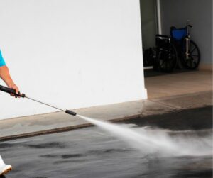 person washing off driveway stains using pressure washer